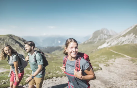 Three cheerful hikers on a mountain ridge with a wide view of peaks in clear summer weather.