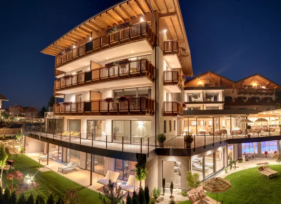 Südtiroler Wellnesshotel mit Holzbalkonen und beleuchteter Gartenanlage bei Nacht
