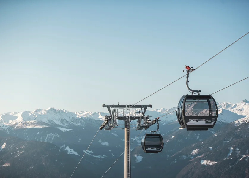 Gondelbahn Meran 2000 mit zwei Kabinen vor verschneitem Alpenpanorama bei klarem Himmel